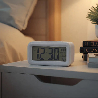 Digital clock on a nightstand with books and a plant, indicating time and date.