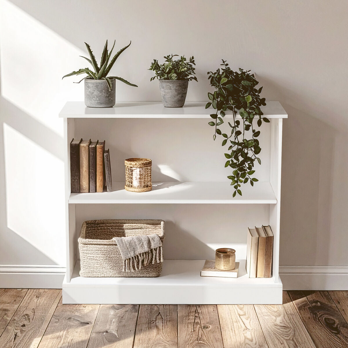 White bookshelf with decorative items including books, a basket, and plants in a room with wooden flooring.