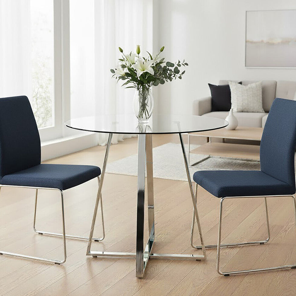 Modern dining area with a round glass table and blue chairs in a bright room.