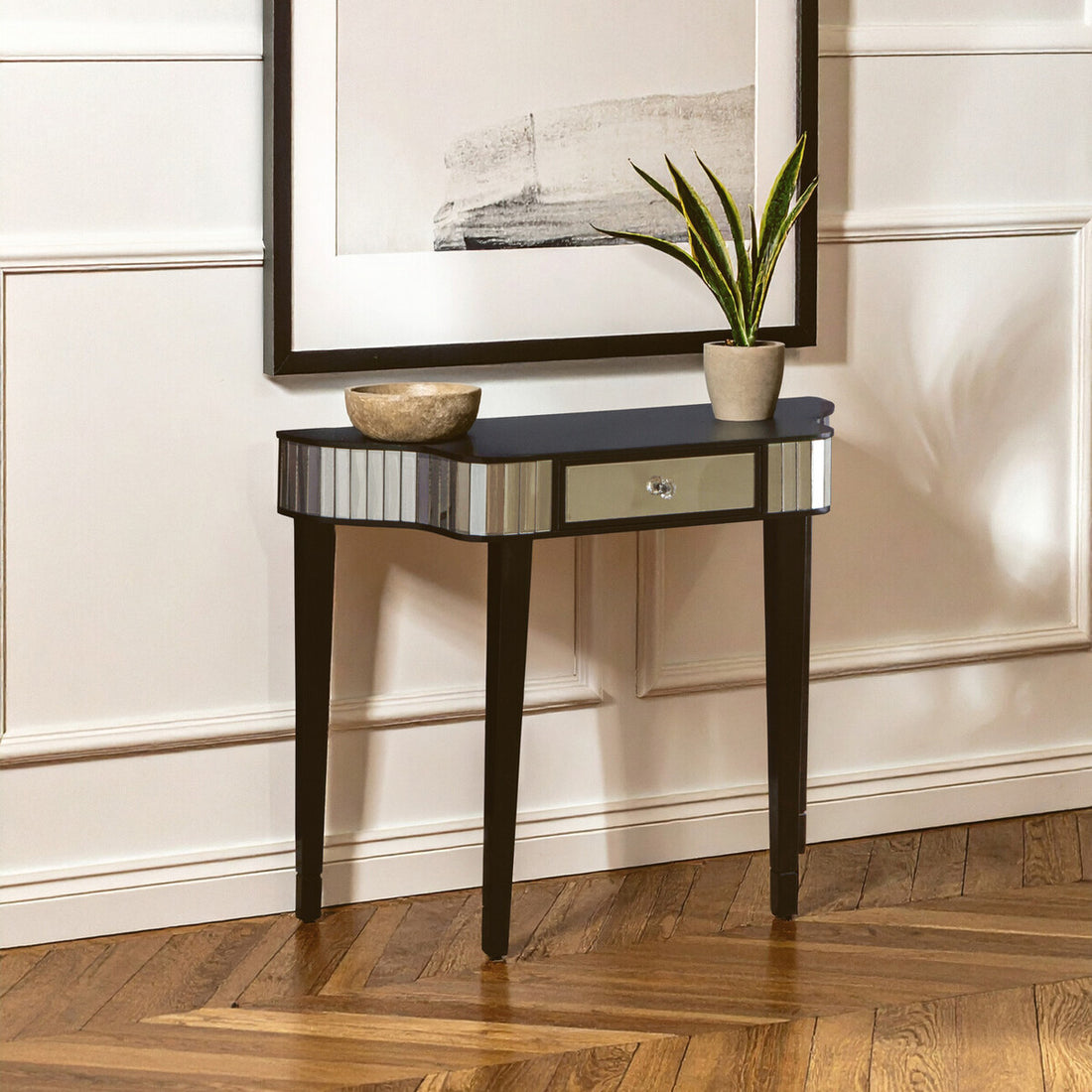 Console table with a mirror surface in a room with a framed picture and plant.