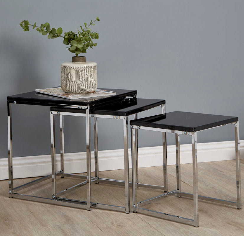 Set of three nesting tables with black tops and silver frames in a room setting.