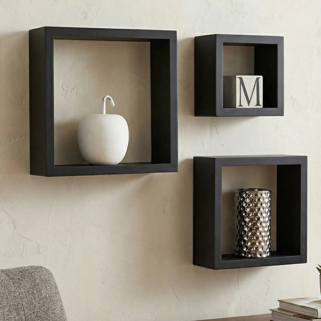 Three black square wall shelves with decorative items on a beige wall.