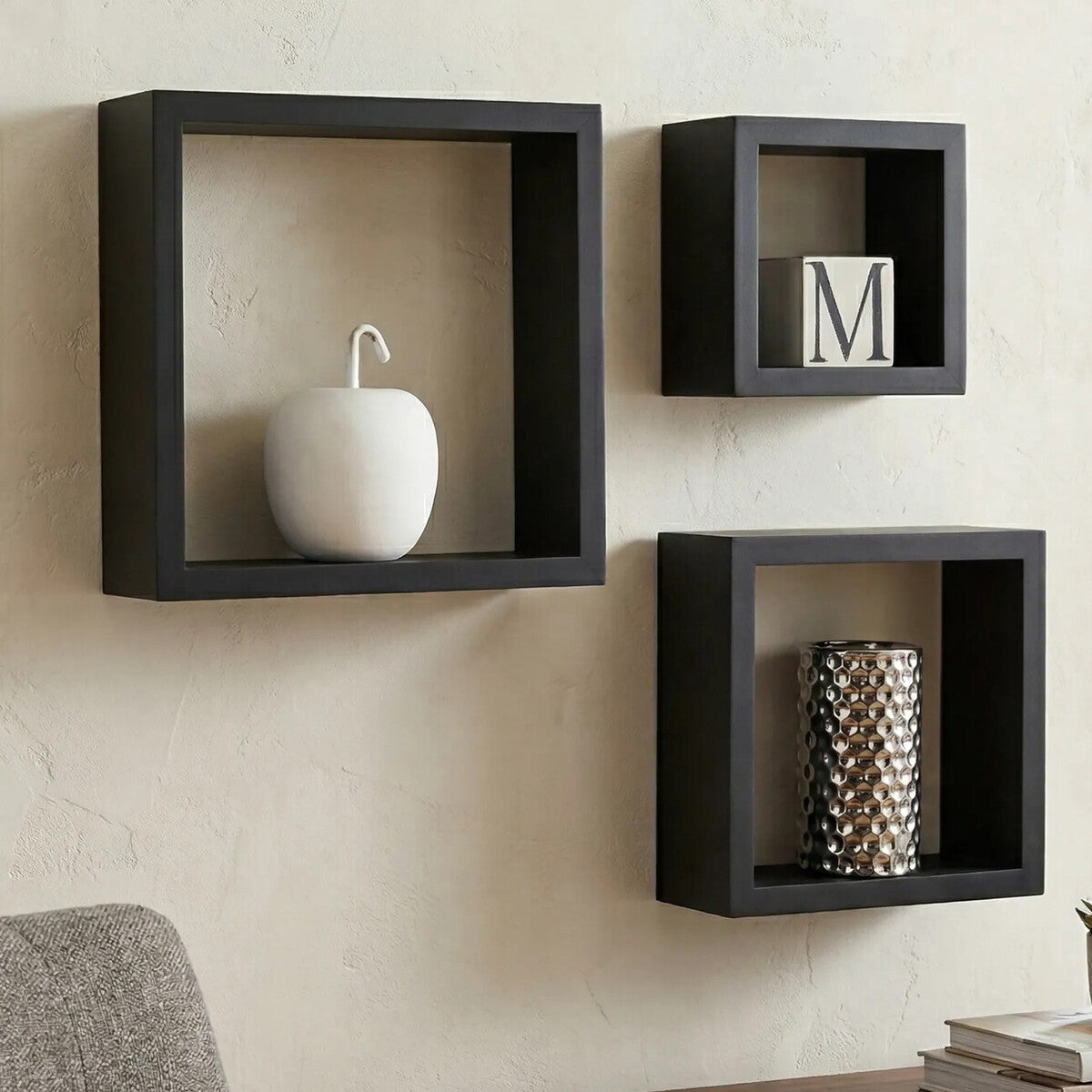 Three black square wall shelves with decorative items on a beige wall.