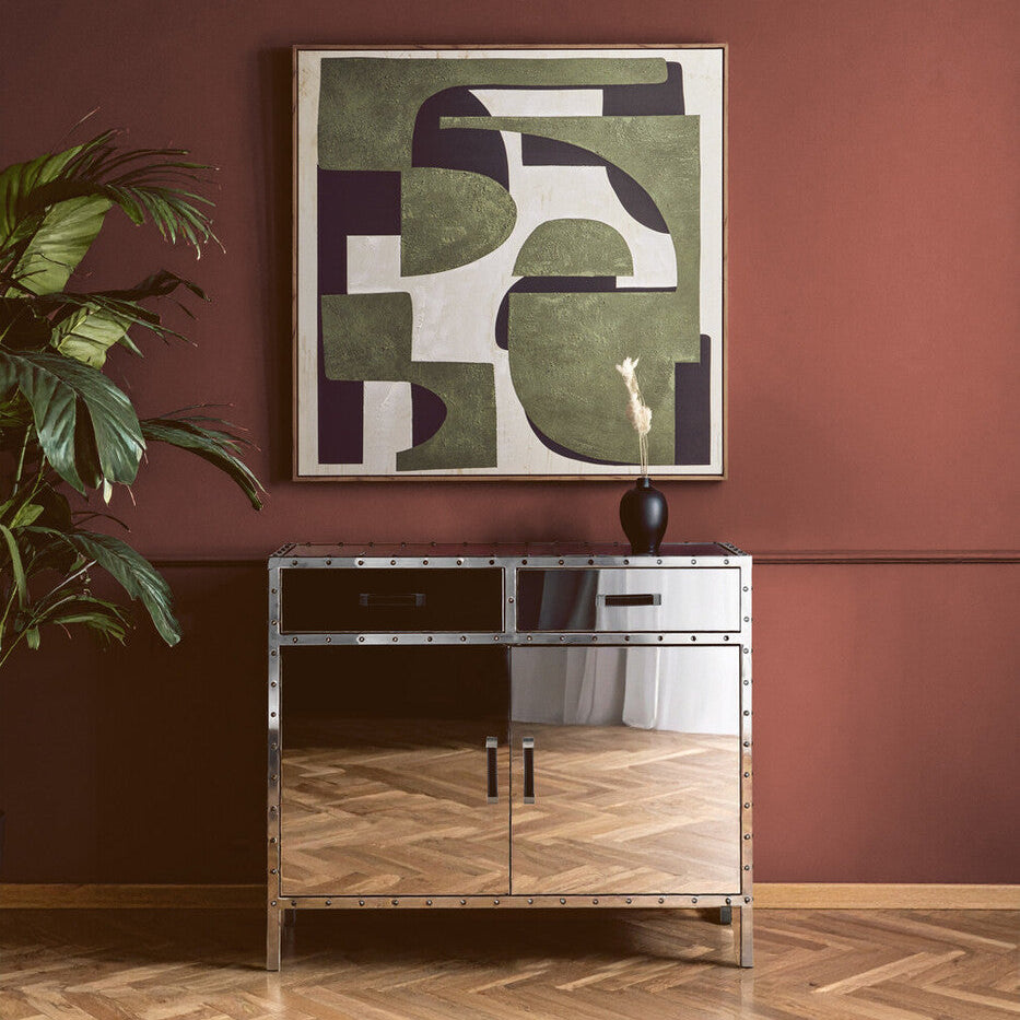 Decorative cabinet with a mirror finish against a red wall with abstract art and a plant.