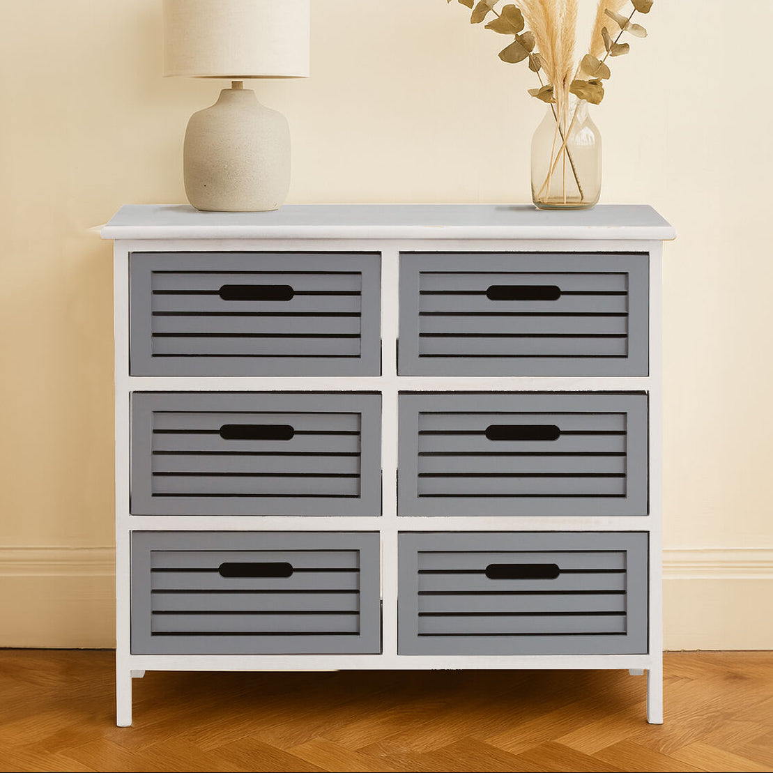 White dresser with six gray drawers against a beige wall.