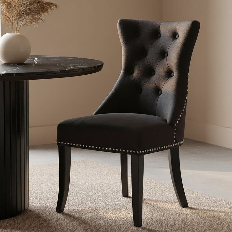 Dark upholstered chair next to a round wooden table with a vase on a beige carpet.