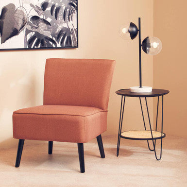 Orange chair and black side table against a beige wall with a leafy artwork.