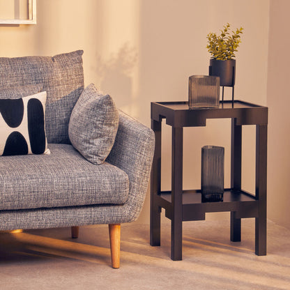 Gray sofa with patterned cushions next to a dark wooden side table with decorative items in a room.