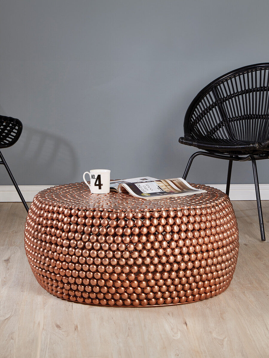 Copper beaded coffee table with a cup and magazine in a room with black chairs.