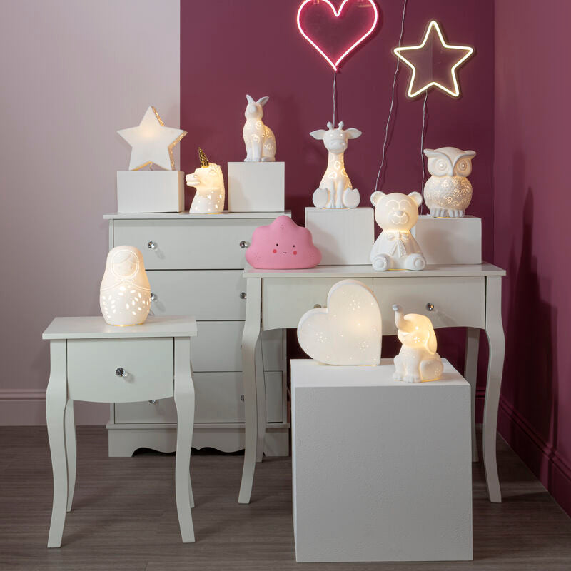 Decorative scene with lit candles, star-shaped lights, and small figurines on a white dresser against a purple wall.