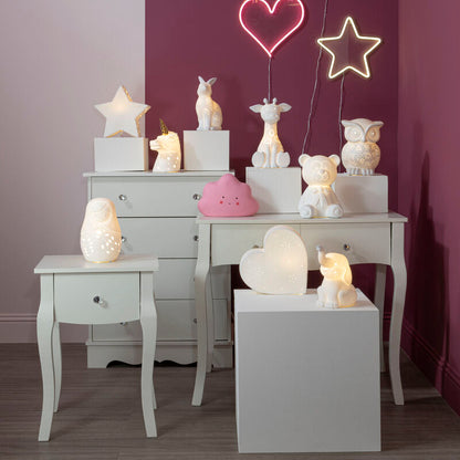 Decorative scene with lit candles, star-shaped lights, and small figurines on a white dresser against a purple wall.