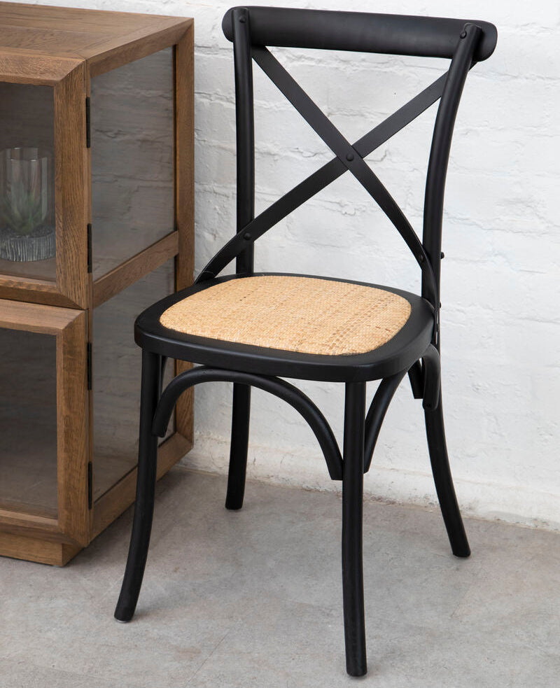 Black metal chair with woven seat against a white brick wall.