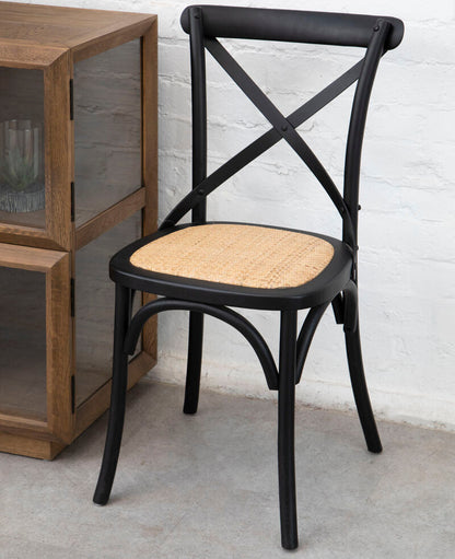 Black metal chair with woven seat against a white brick wall.
