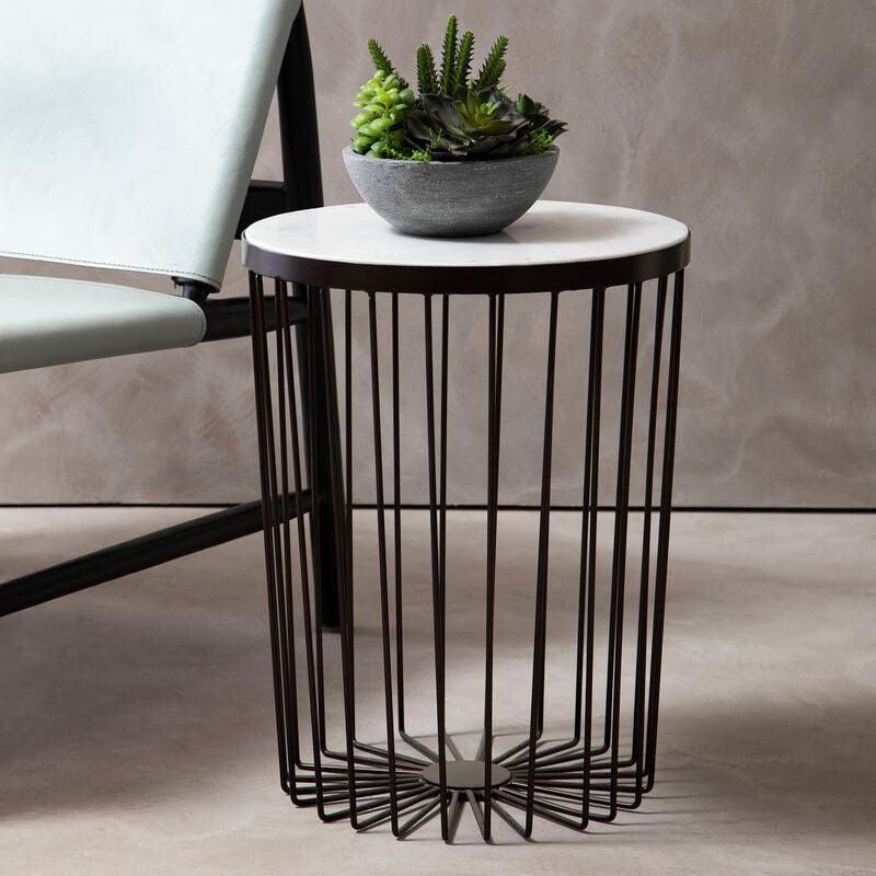 Modern side table with black metal base and white marble top, featuring a potted plant, next to a gray chair.
