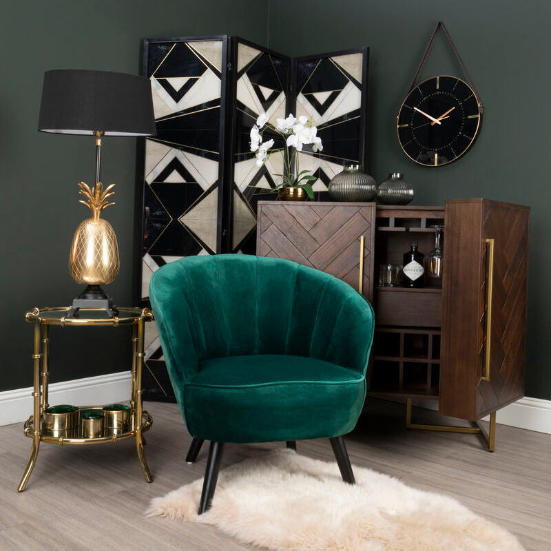Modern interior with a green velvet chair, gold lamp, and decorative wall piece.
