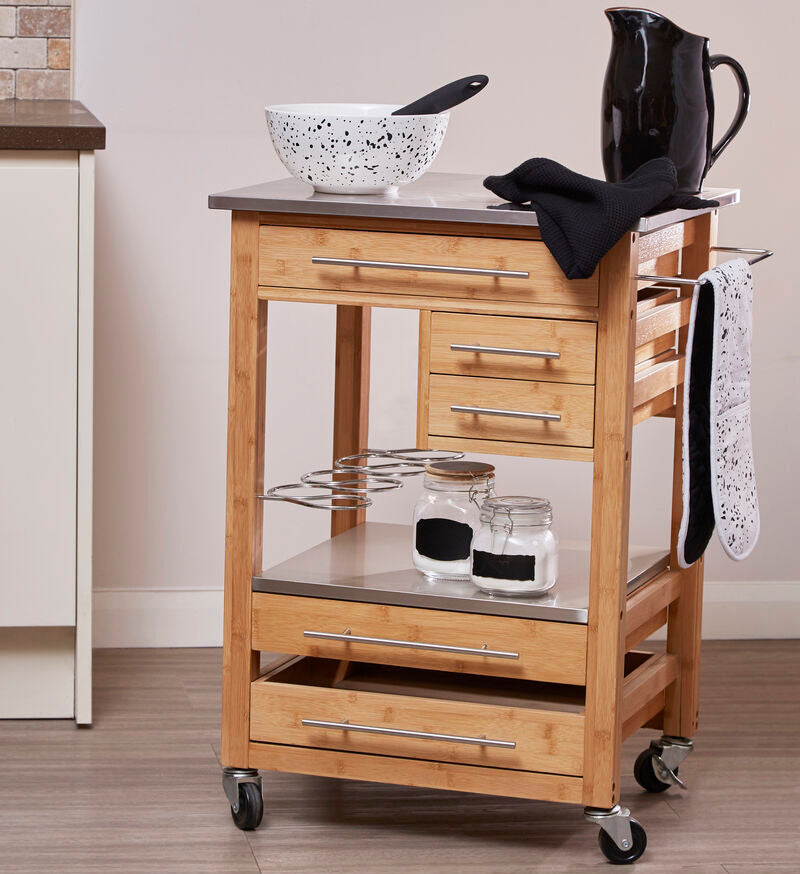 Wooden kitchen cart with stainless steel top and various kitchen items in a kitchen setting.
