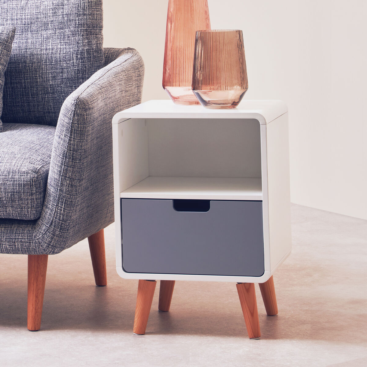 White side table with a gray drawer next to a gray armchair.