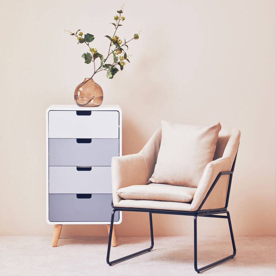 Modern chair with cushions next to a white dresser with gray drawers against a beige wall.