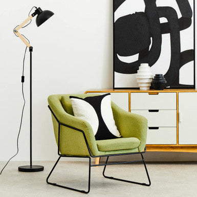 Modern interior with a green chair, black floor lamp, and abstract art on a white wall.