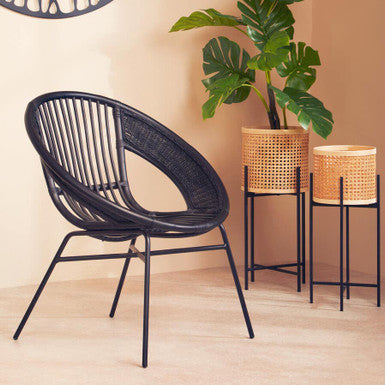 Black wicker chair in a room with a plant and baskets on a light wood floor.
