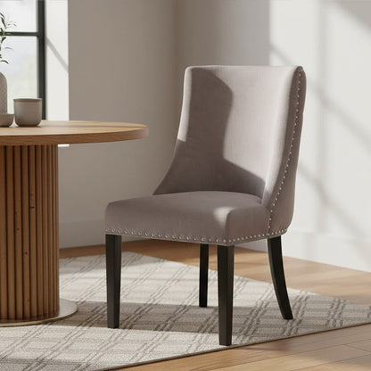 Gray upholstered chair with nailhead trim next to a wooden table in a bright room.