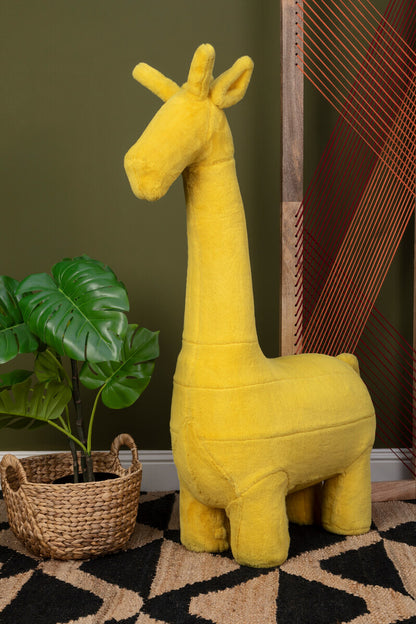 Yellow plush giraffe toy on a patterned rug with a plant and woven basket in the background.