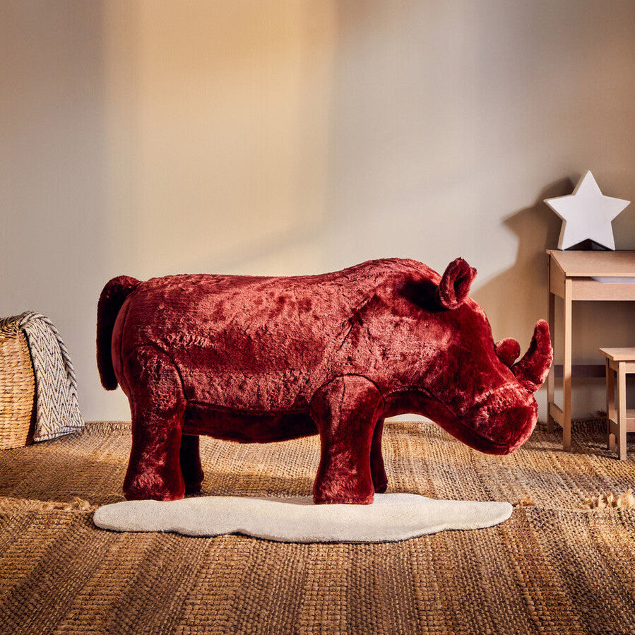Red rhinoceros plush toy on a textured surface with a star decoration in the background