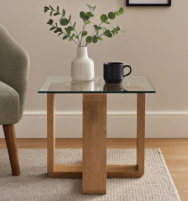Glass side table with wooden legs holding a vase and a mug, with framed plant pictures on the wall.