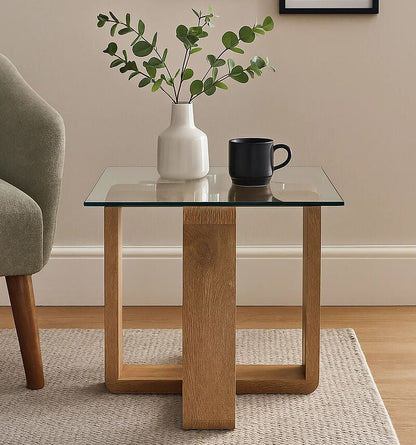 Glass side table with wooden legs holding a vase and a mug, with framed plant pictures on the wall.