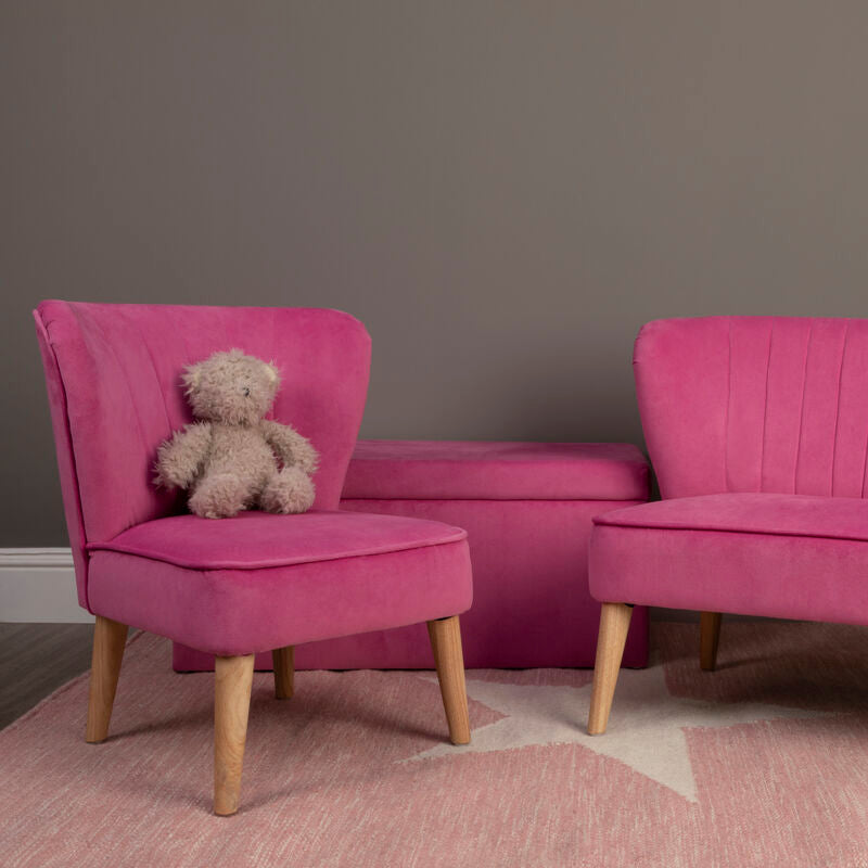 Pink velvet chair and loveseat with a teddy bear on the chair against a gray wall.