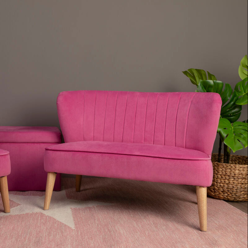 Pink velvet chair and loveseat with a teddy bear on the chair against a gray wall.