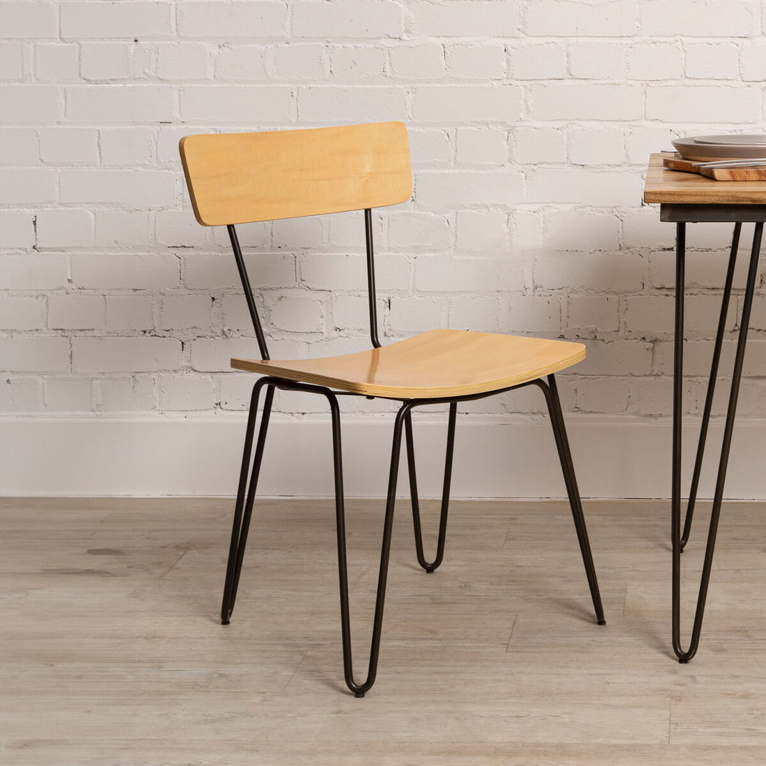 Wooden chair with black metal legs against a white brick wall.