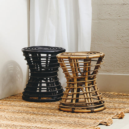 Two woven stools, one black and one brown, on a textured surface with a white curtain in the background.