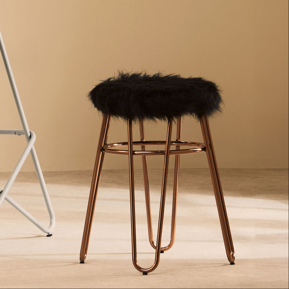 Bar stool with black fur cushion and metal legs against a beige wall.