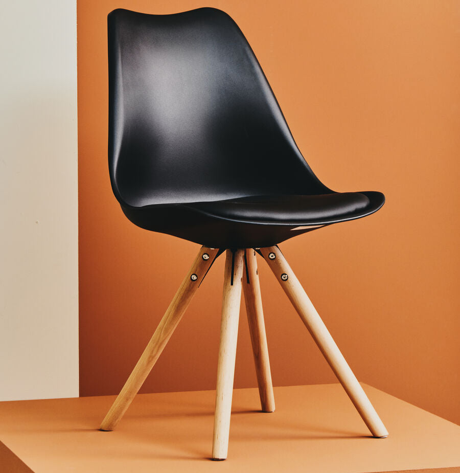 Black chair with wooden legs on an orange platform against a brown wall.