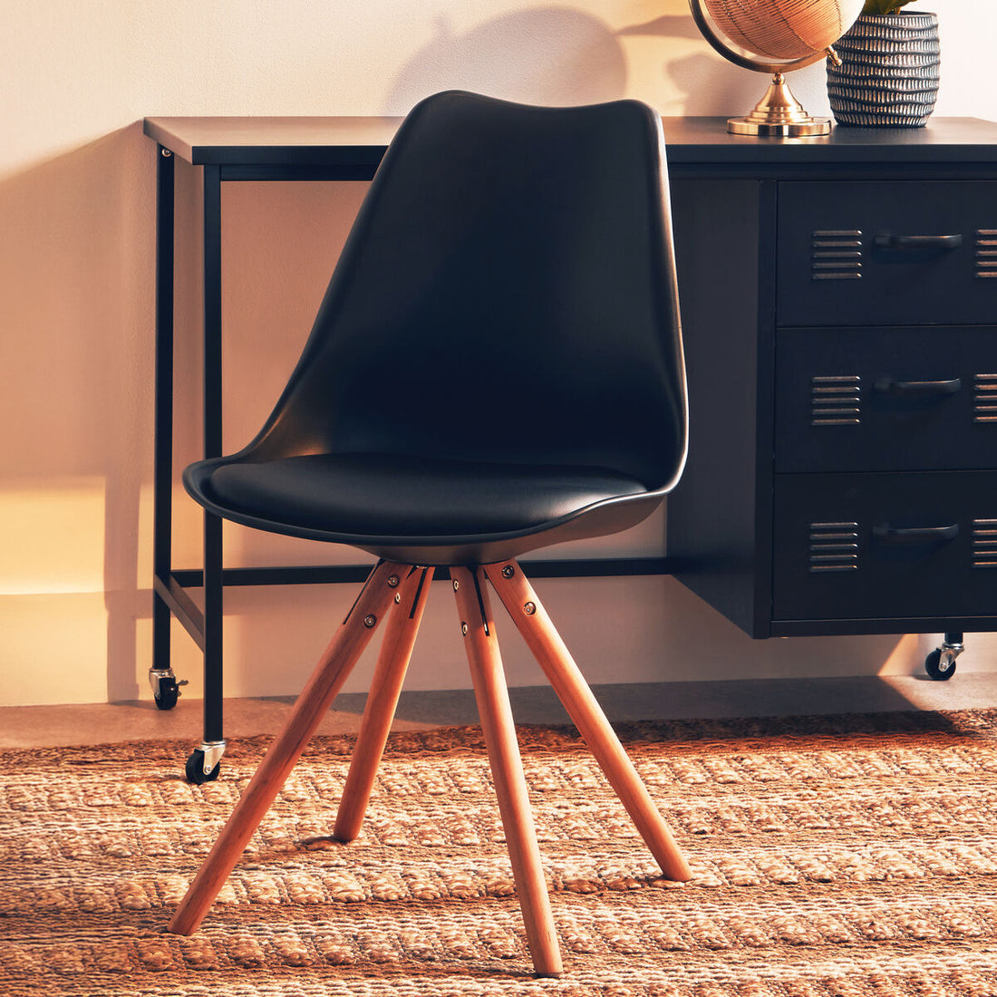 Black chair with wooden legs in a room with a desk and decorative items.