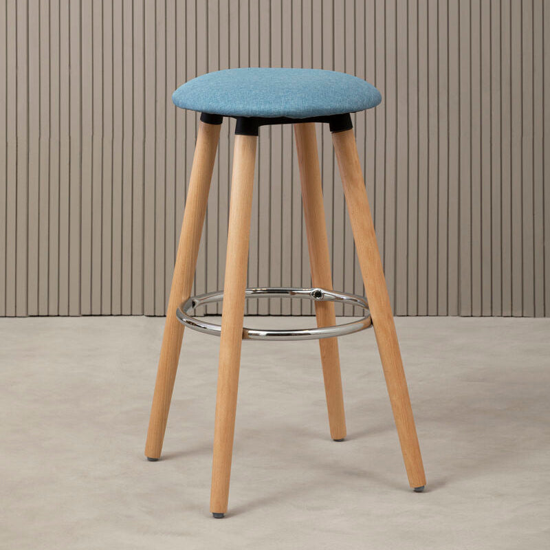 Bar stool with blue cushioned seat and wooden legs against a striped wall.