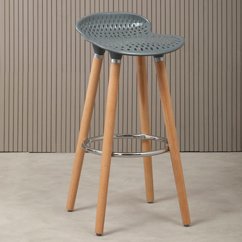 Bar stool with a perforated backrest and wooden legs against a striped wall.