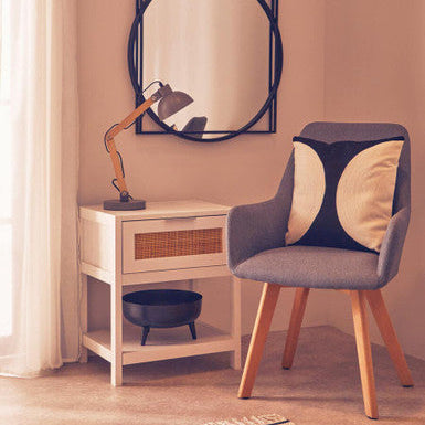 Modern chair with a decorative cushion next to a side table with a lamp and mirror in a room.