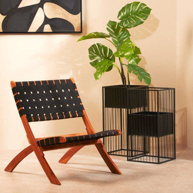 Modern chair with woven backrest in a room with a plant and abstract wall art.