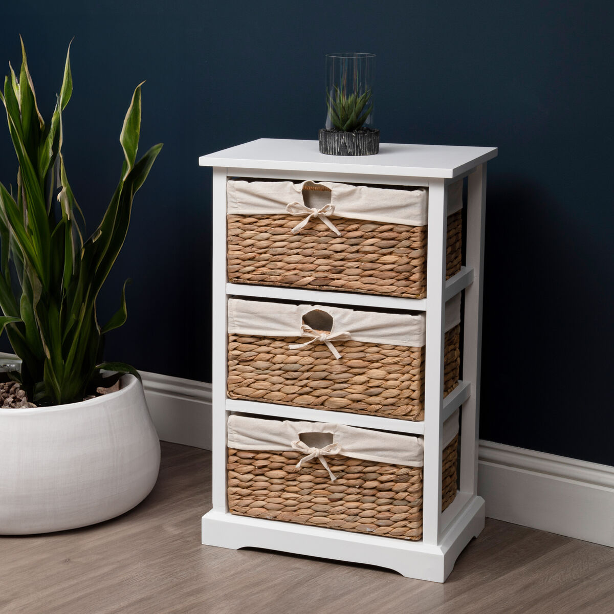 White cabinet with wicker drawers next to a potted plant against a dark wall.