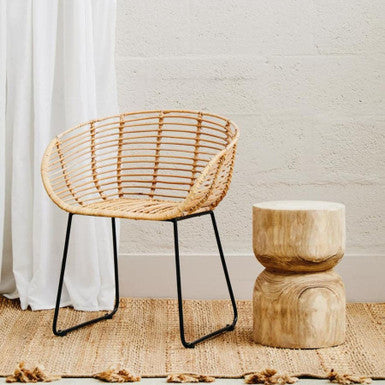 Woven chair with black legs and a wooden side table against a white wall.