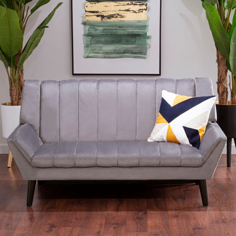 Gray sofa with a colorful pillow in a room with plants and a framed abstract painting on the wall.