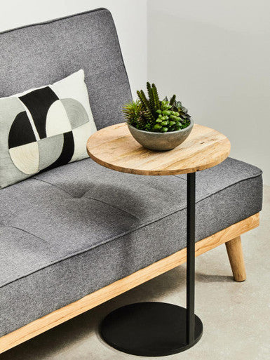 Small round wooden side table with black base next to a gray sofa with a decorative pillow.
