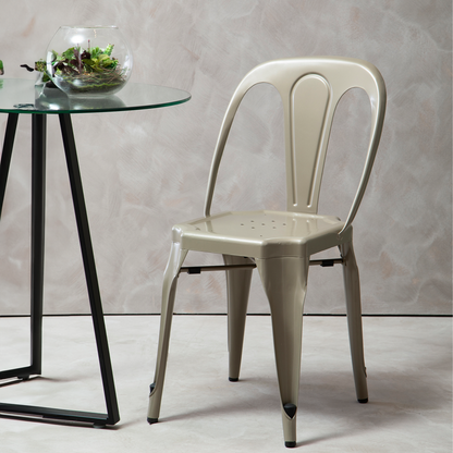 Beige metal chair next to a glass table with a plant on a light gray background