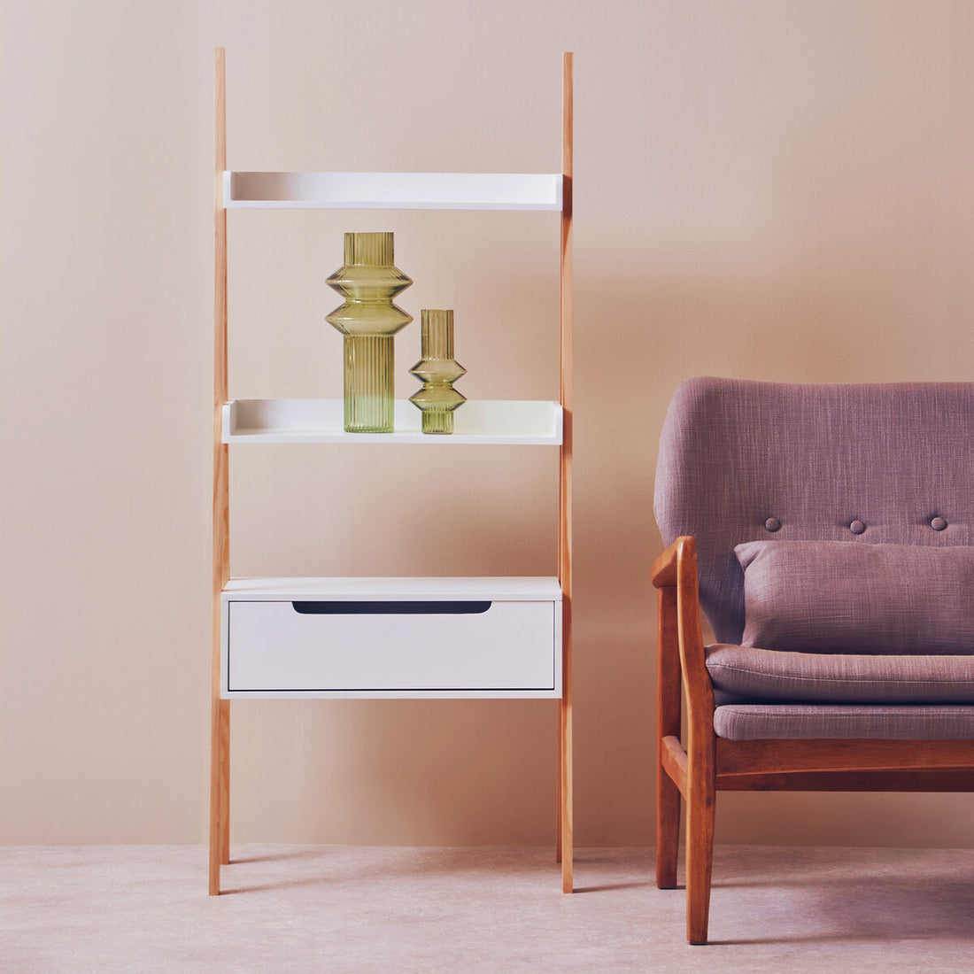 Tall wooden shelf with white shelves and a drawer next to a purple armchair against a beige wall.