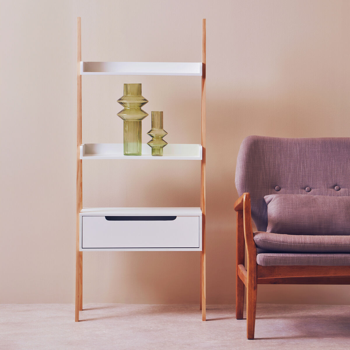 Tall wooden shelf with white shelves and a drawer next to a purple armchair against a beige wall.