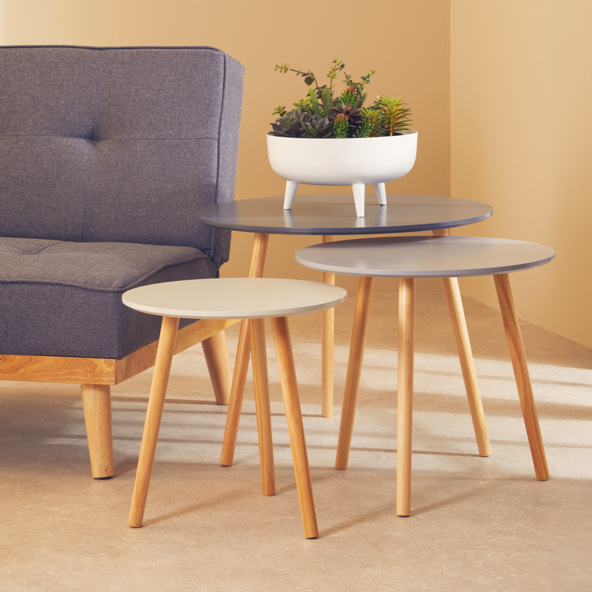 Set of three round tables with wooden legs in a living room setting.