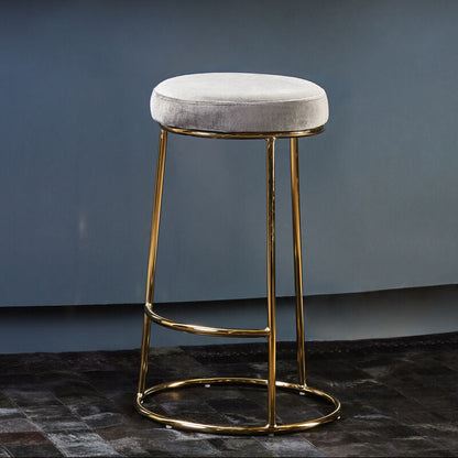 Bar stool with gold legs and gray cushioned seat in front of a blue wall.