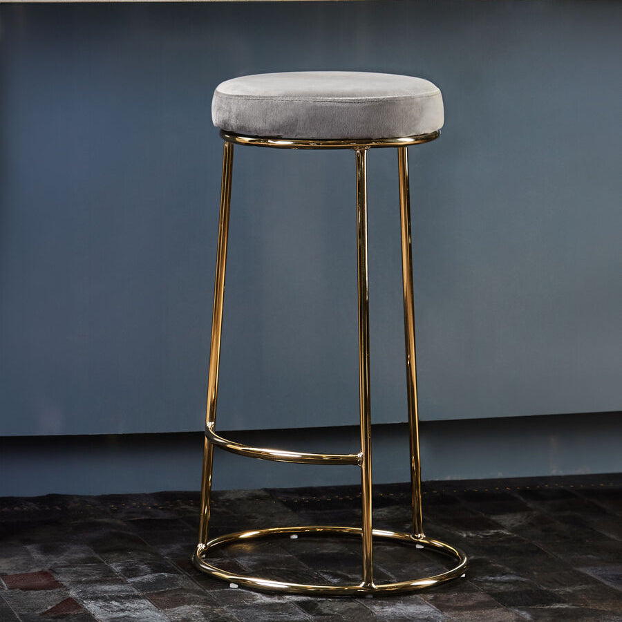 Gray cushioned bar stool with gold legs in front of a white countertop against a blue wall.